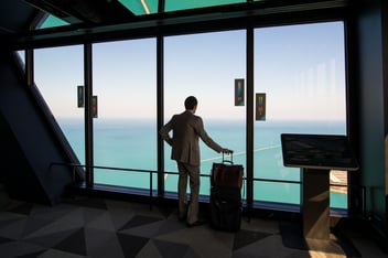 Man dressed in suit holding a suitcase handle looking out to the ocean