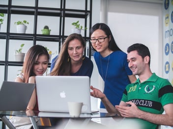four workers smiling in front of a computer 